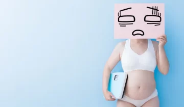 chubby-woman-holding-scale-and-sign-to-cover-face